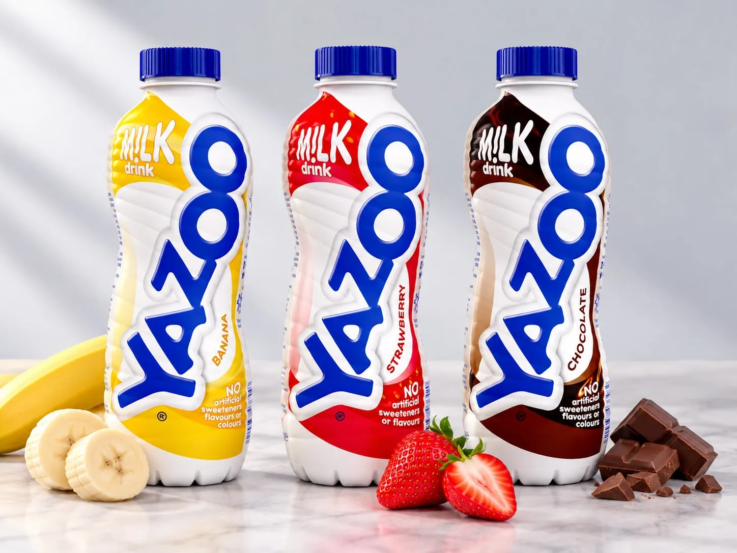 Three Yazoo milk drink bottles: banana, strawberry and chocolate, with banana slices, strawberries and chocolate pieces.